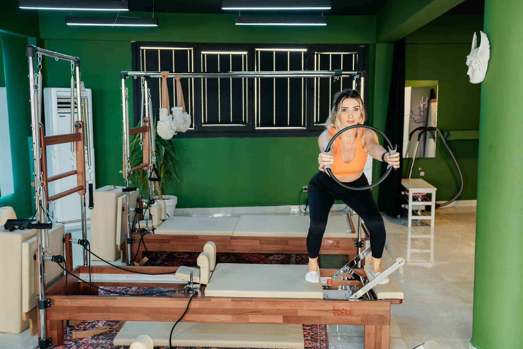 Estudio de pilates con reformers y muros verdes, dos personas entrenando